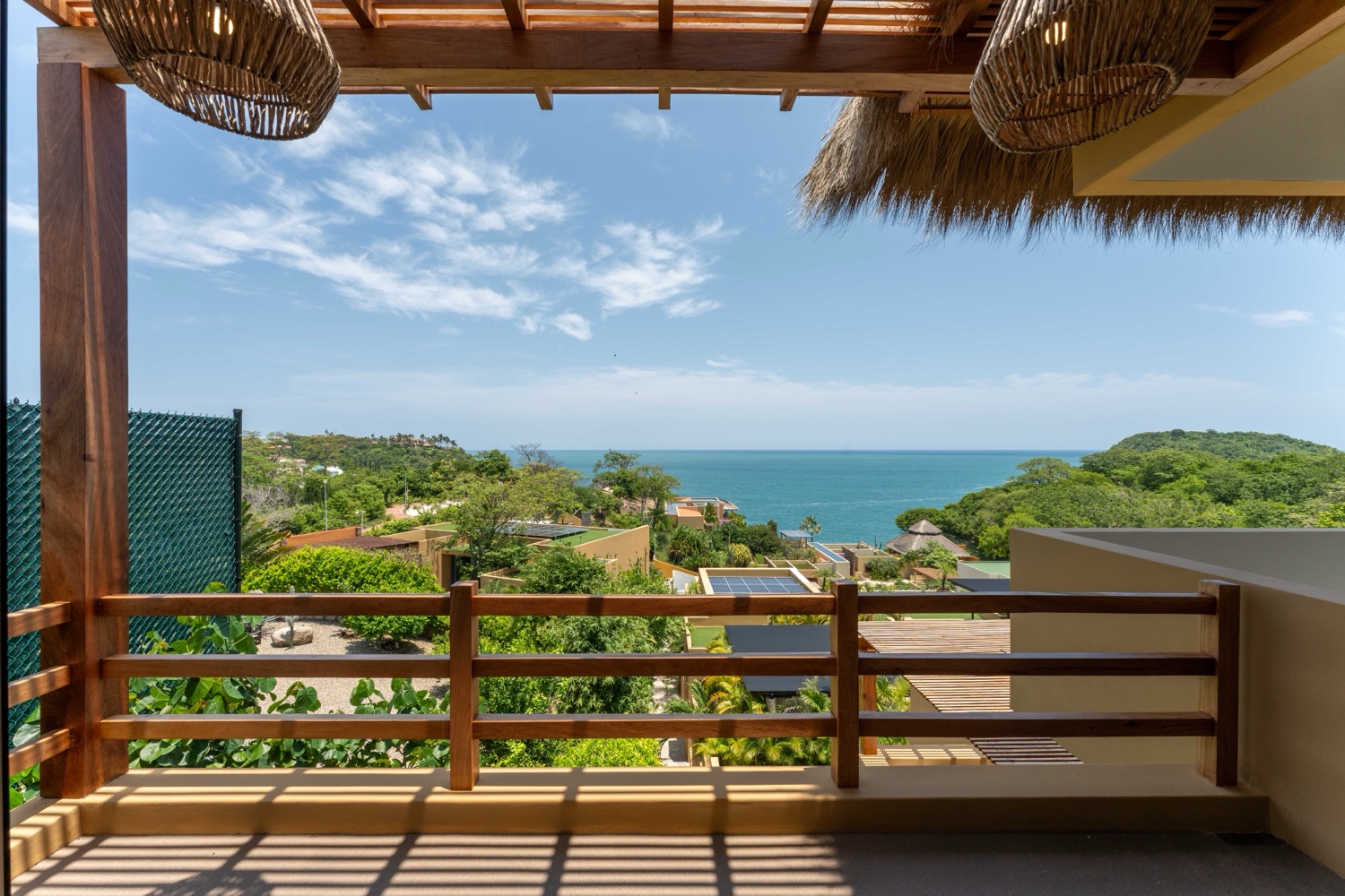 Balcón con pérgola de madera y vista al mar entre vegetación