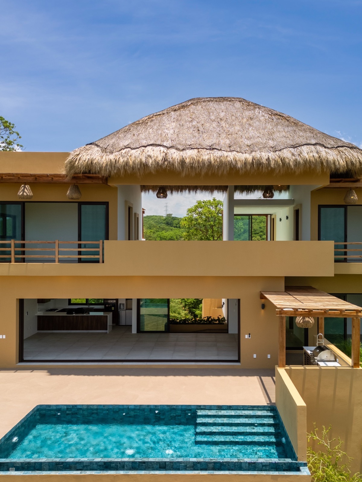 Fachada de residencia de lujo con techo de palapa y alberca infinita